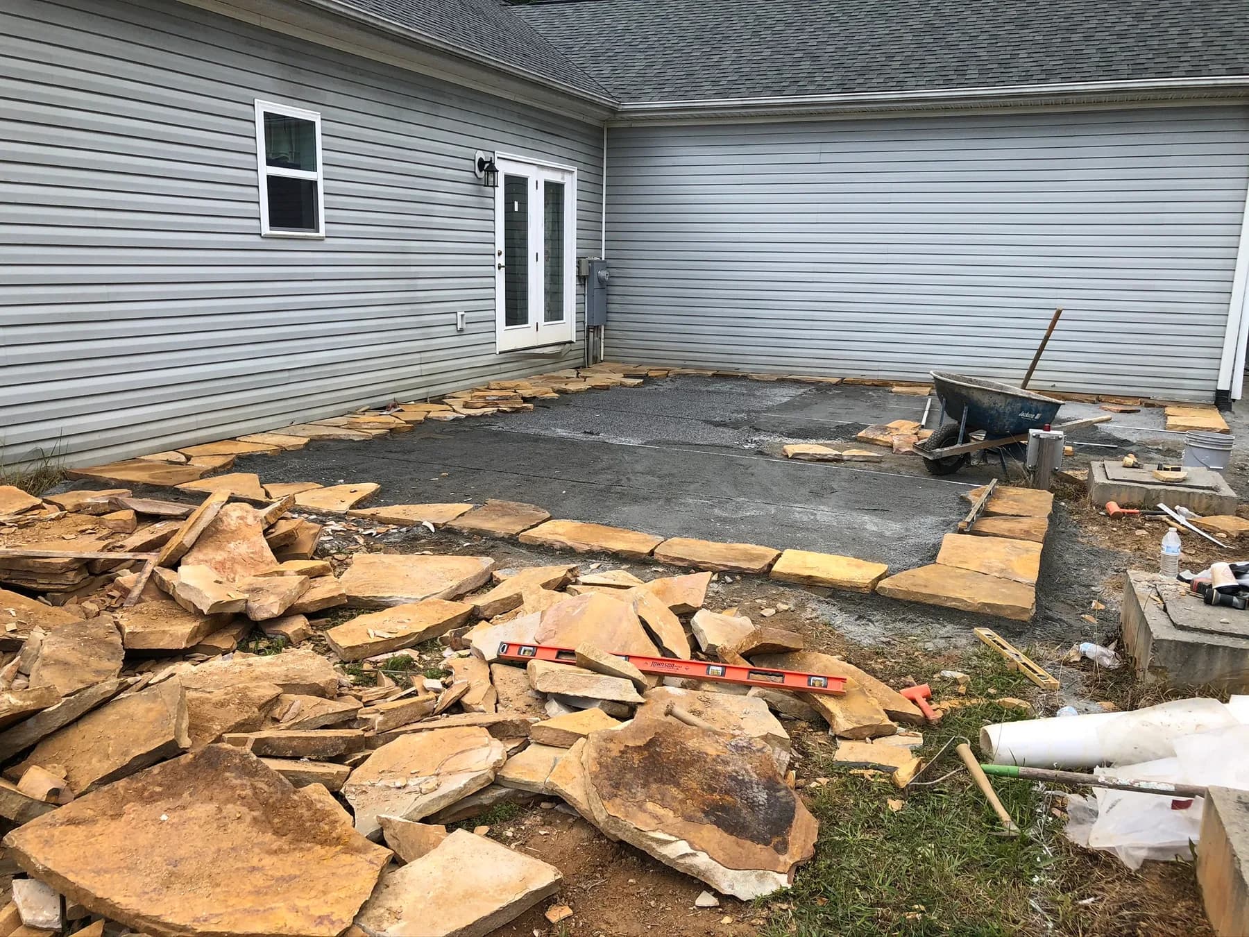 Natural stone patio installation in progress along a residential foundation, view 4