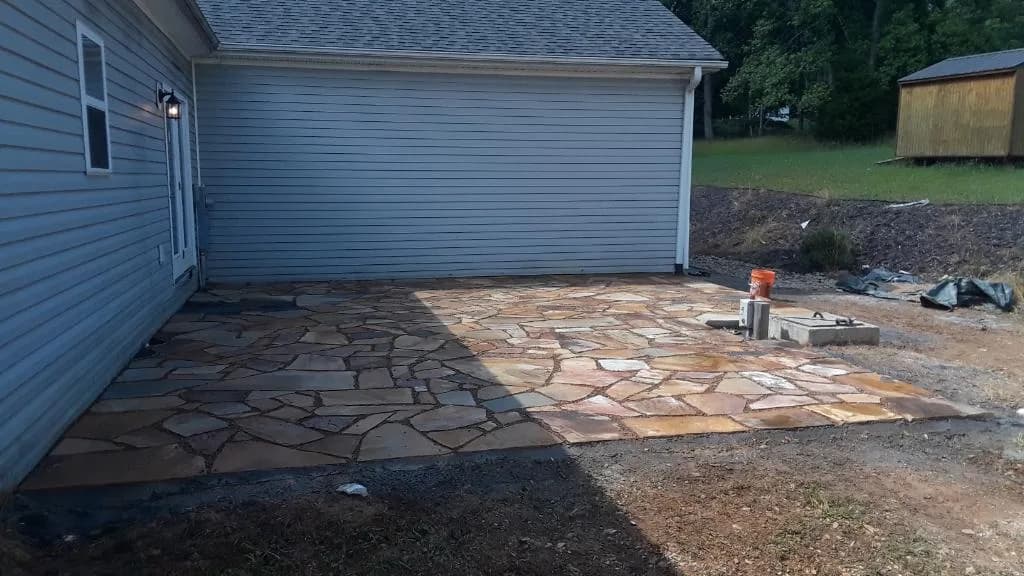 Natural stone patio field in progress beside a residential garage wall