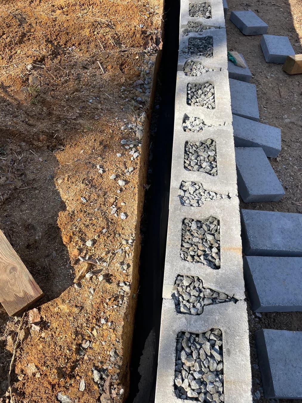 Retaining wall construction with block, drainage stone, and prepared trench