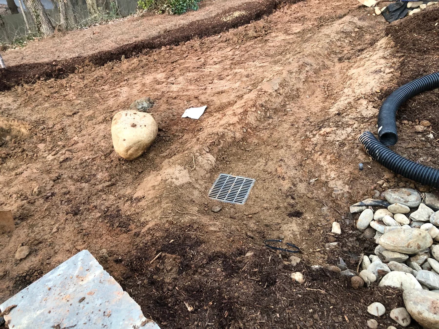 Drainage preparation with catch basin, stone, and pipe routing in a residential landscape area, view 1