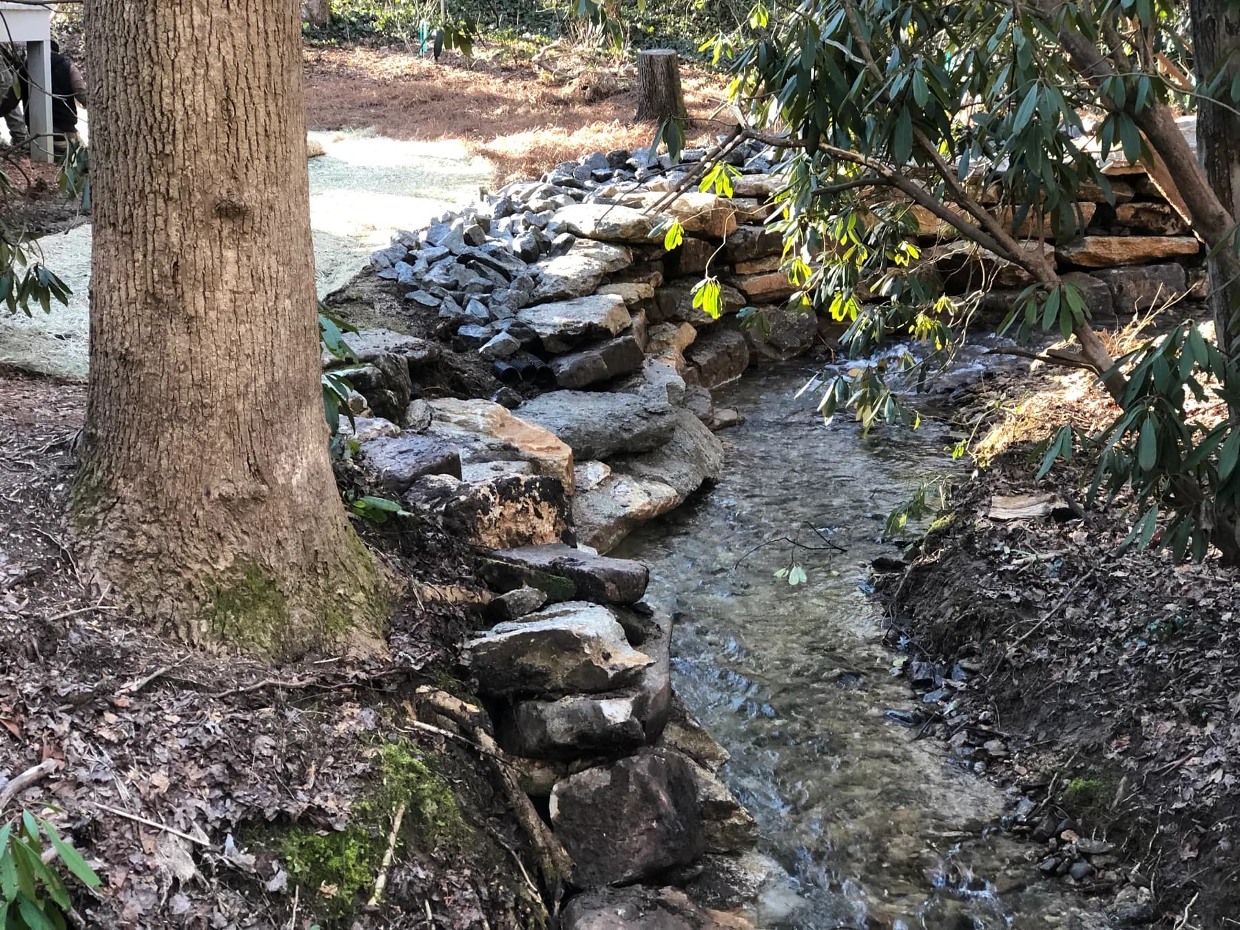 Stone-lined riverbank edge with active water flow and natural bank conditions, view 1