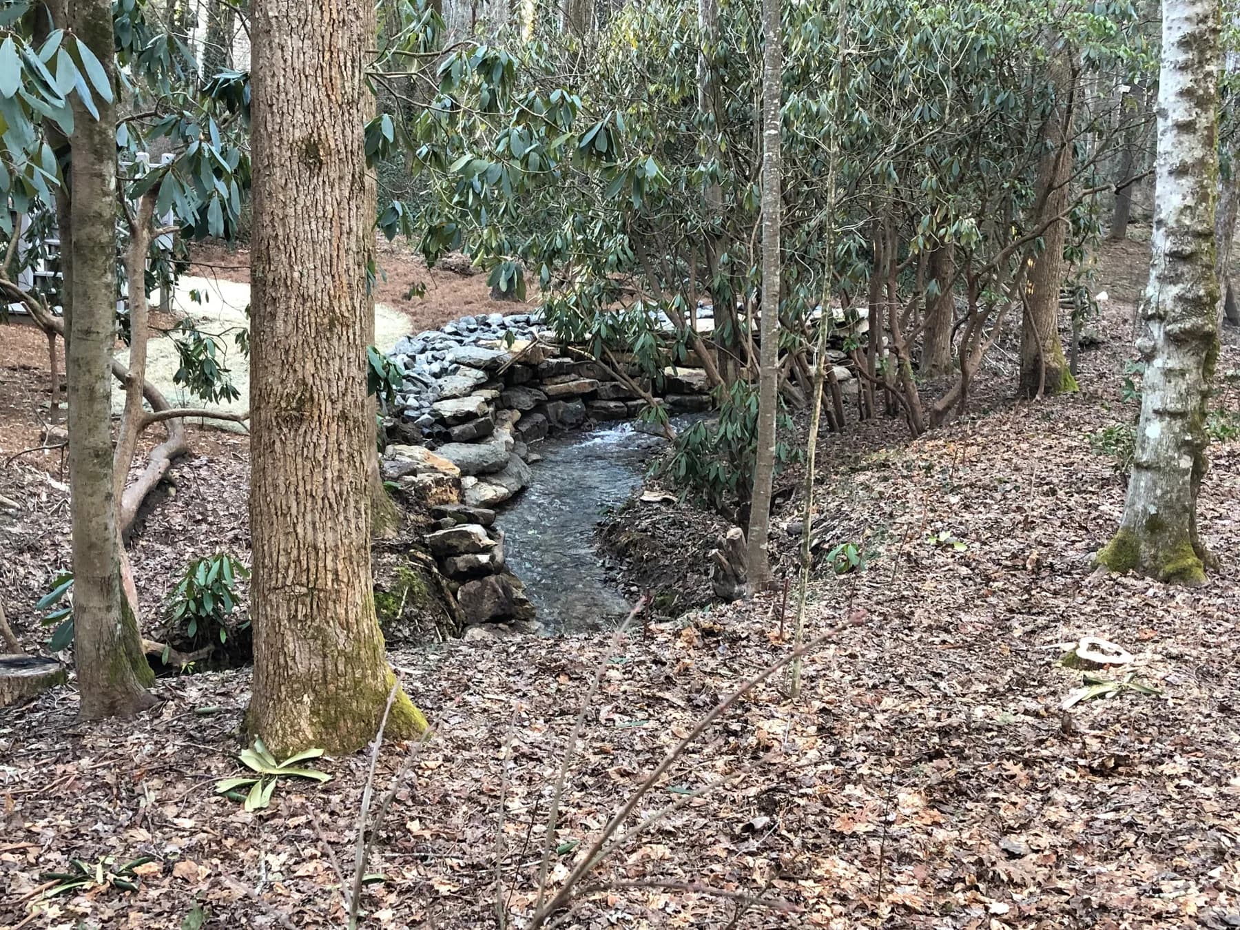 Completed riverbank erosion-control stonework in a wooded stream setting, view 5