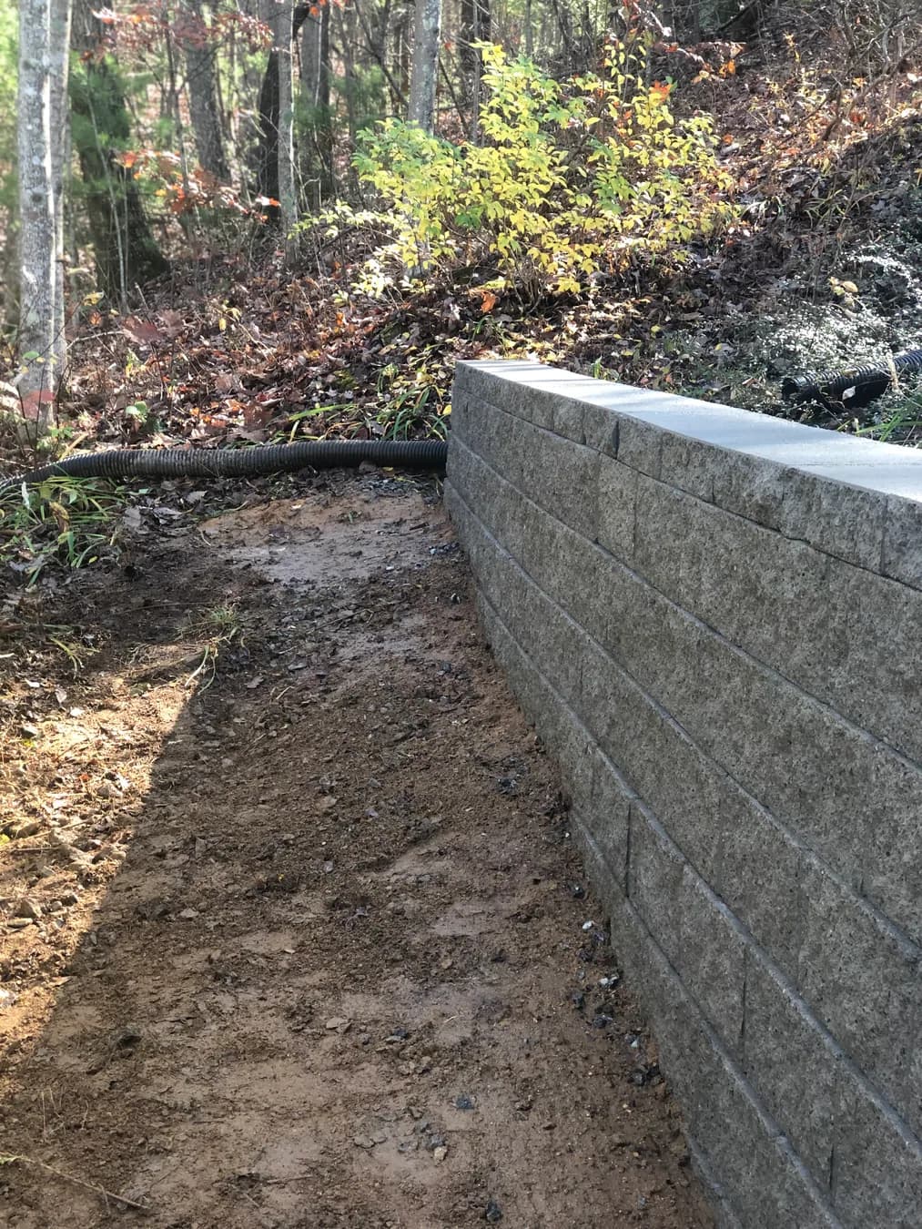 Finished segmental retaining wall with clean wall line and wooded backdrop, view 4