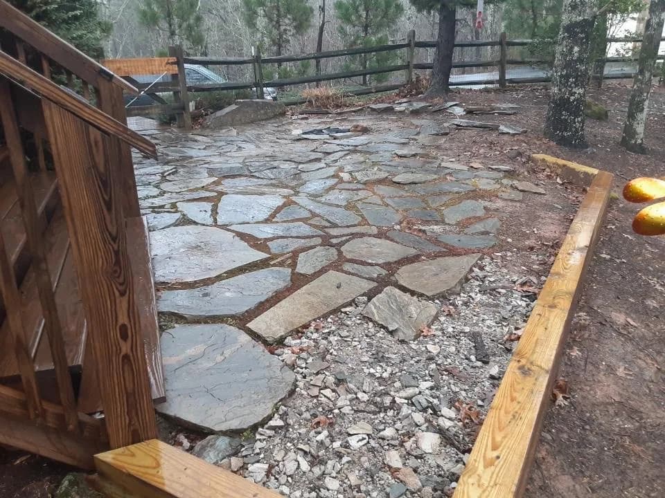 Natural stone patio installation with stone surface and gravel joints near a deck edge, view 1