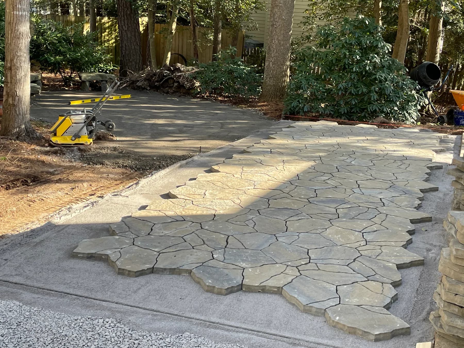 Paver field and border courses being laid in wooded backyard